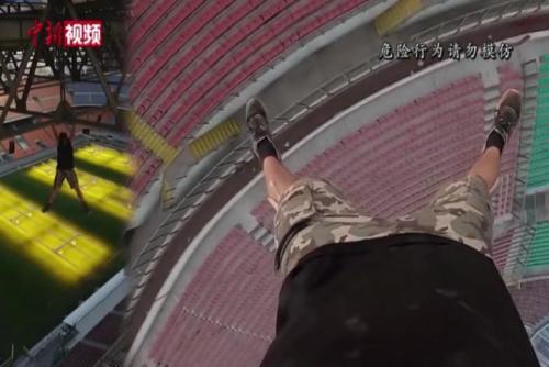 英国小伙为寻刺激徒手爬上体育场顶棚 悬挂在金属架上