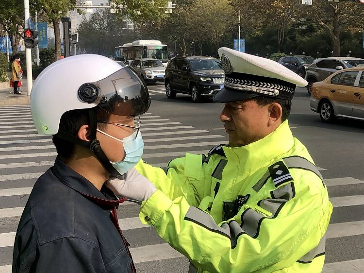 青岛交警宣传“一盔一带”，为市民送上头盔和挪车电话贴