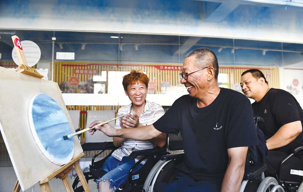 在威海长城爱心大本营，油画师王刚（左）指导残疾人学员进行油画创作。