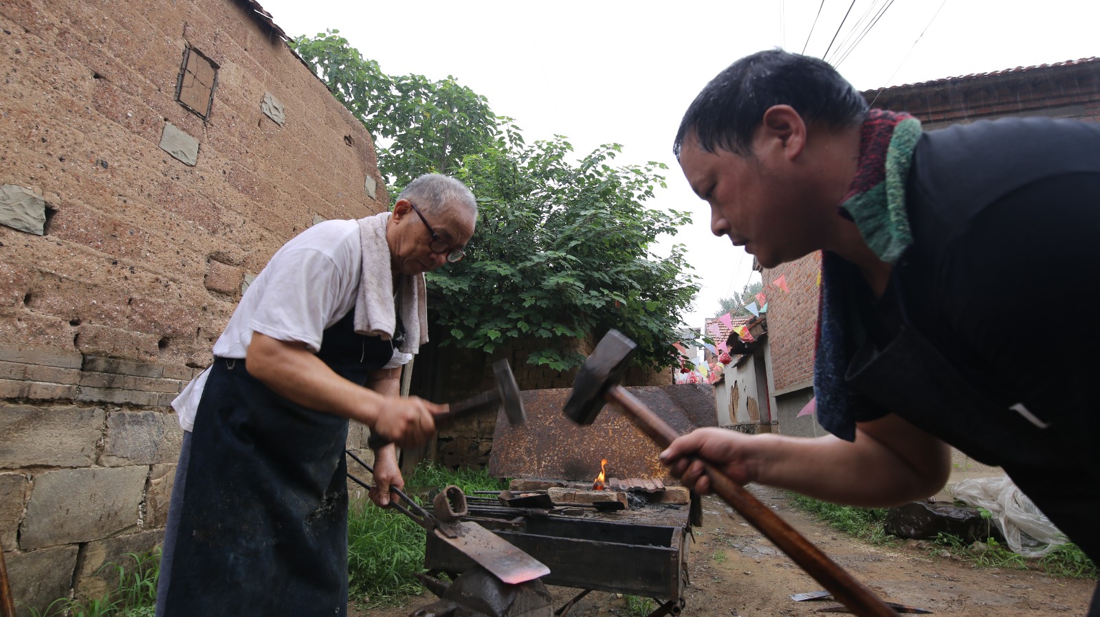 铁匠牛祺圣(左),牛大伟(右)在村头支上烘炉为村民修理农具(撅头).